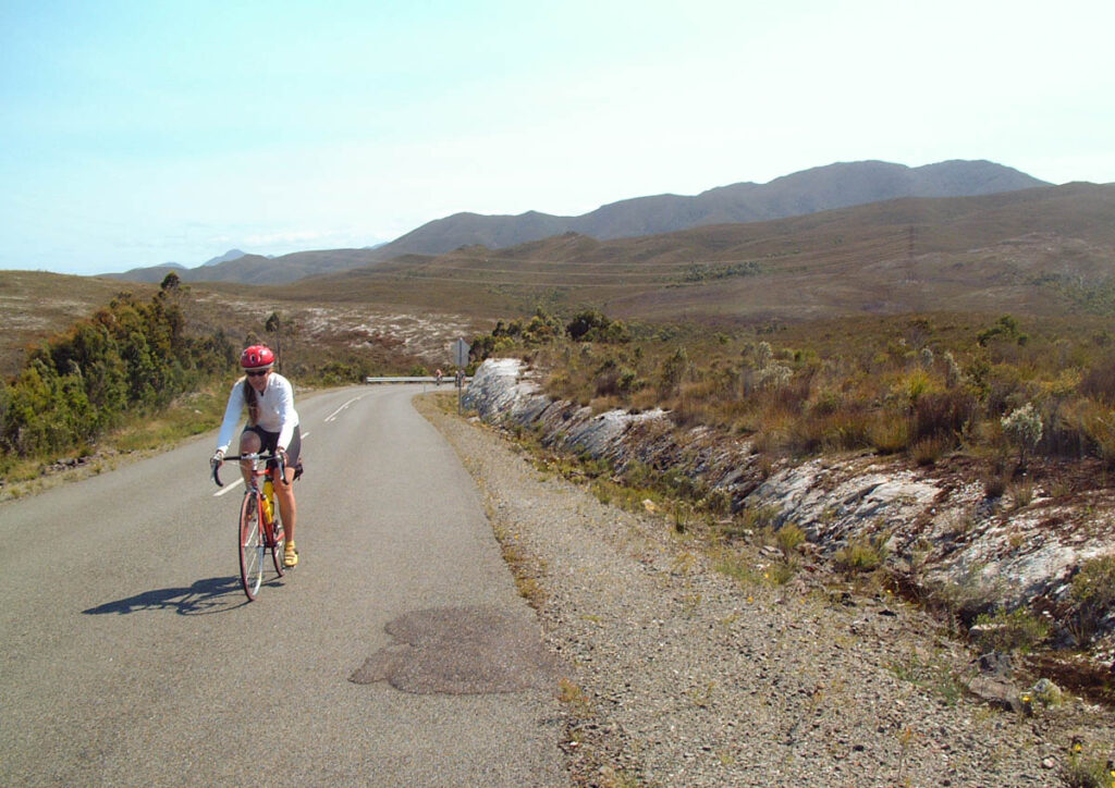 Woman climbing a steep hill on a bike, with two riders far in the background