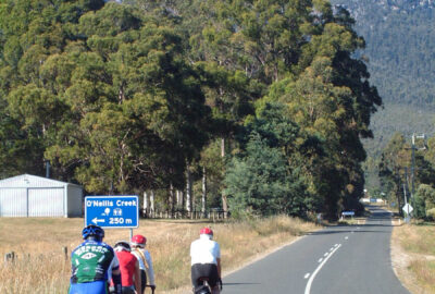Four cyclists riding on the left side of a long road with no cars, with granite mountains in the distance