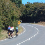 Four cyclists riding on the left side of a curving road with no traffic