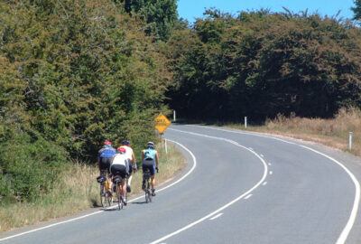 Four cyclists riding on the left side of a curving road with no traffic